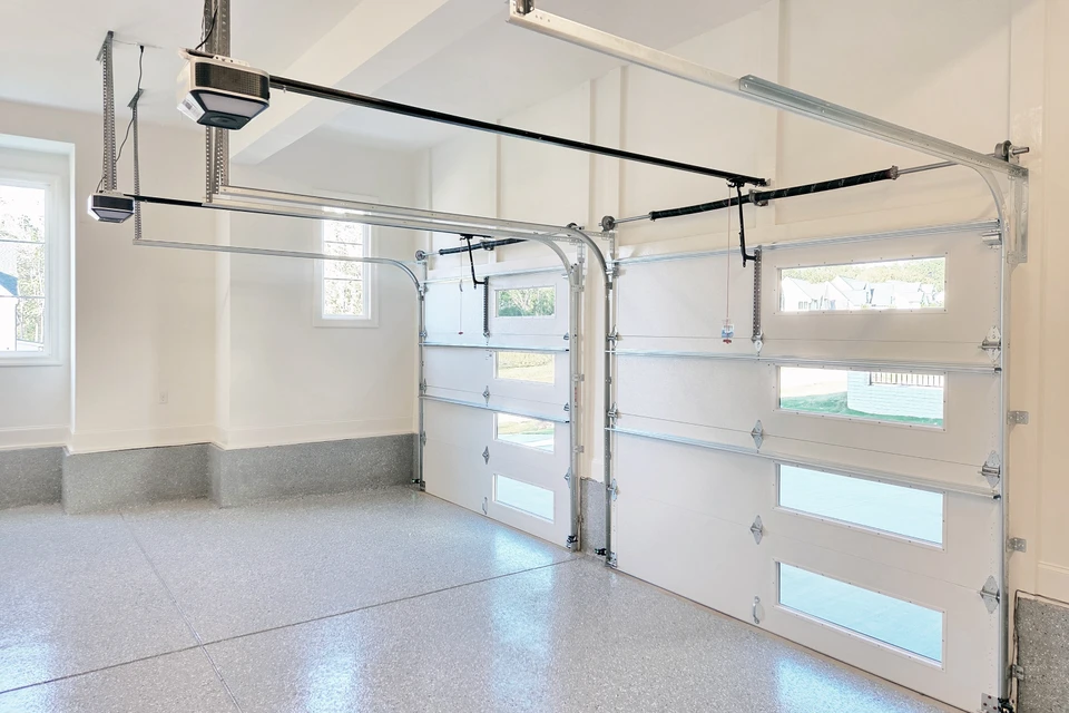 Façade extérieure moderne d'une maison contemporaine avec porte de garage sectionnelle anthracite et portillon assorti intégrés dans un mur en béton beige